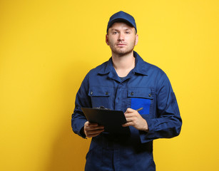 Wall Mural - Young mechanic in uniform with a clipboard standing on a yellow background