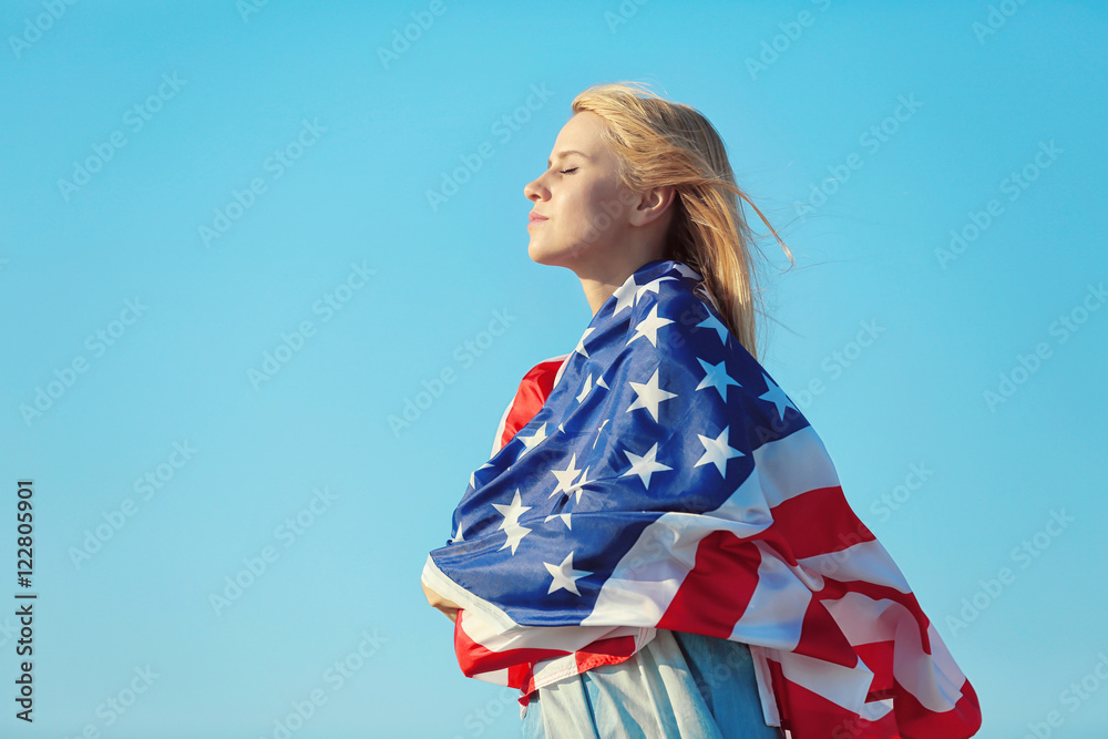 Young woman holding American flag on blue sky background
