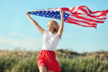 Young woman holding American flag on blue sky background