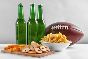 Wall Mural - Rugby ball, snacks and bottles of beer on table against light background