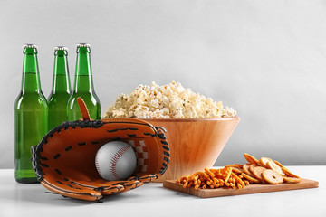 Wall Mural - Baseball glove, snacks and bottles of beer on table against light background