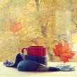 autumn warming drink/ red mug in a woolen scarf is on the table by the window with traces of rain drops 