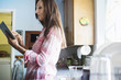 © Mint Images - Senior woman with long brown hair standing in a kitchen, using a digital tablet.