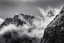 Black And White Photo Of Snow Covered Rocky Mountain Peaks With Fog