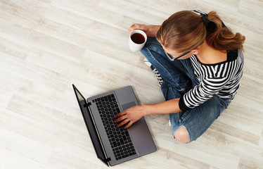 Young woman with coffee mug sitting on the floor with laptop. Concept of distant work, lifestyle and technology.