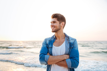 Cheerful young man standing with hands crossed on the beach