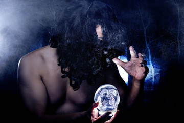 Primitive looking man in a dark smoky forest as a witch doctor or shaman.  The mans face is hidden by hair.  The image depicts Halloween.