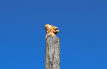 Figurine squirrel with a nut from a tree on a tree stump on a background of blue sky. Figures of animals made of wood. Woodcarving