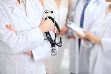 Female doctor holding a stethoscope in his hand, two doctors and patient are on the background