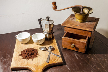 still life with a white two cups and two steel little spoons beside a pile of coffee powder  in the background a vintage coffee mill and an old coffee machine (moka)