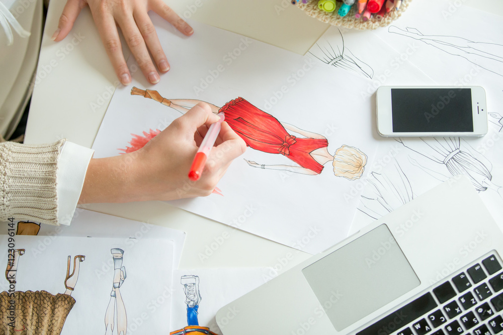 Hands colouring a clothing design sketch in red. Concept photo, top ...