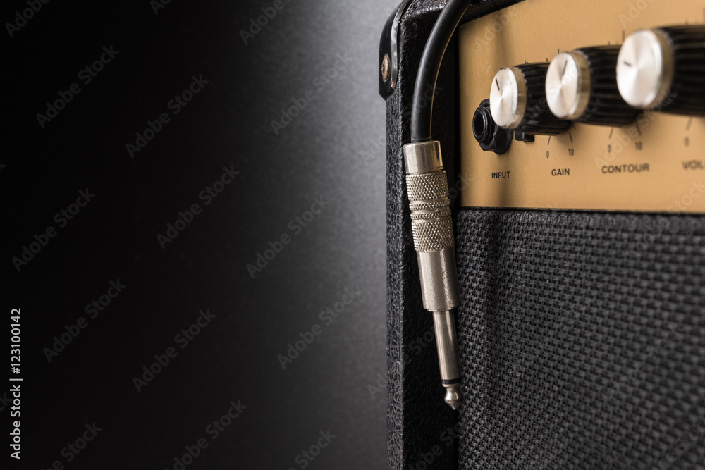 Black guitar amplifier with jack cable on black background - obrazy, fototapety, plakaty 