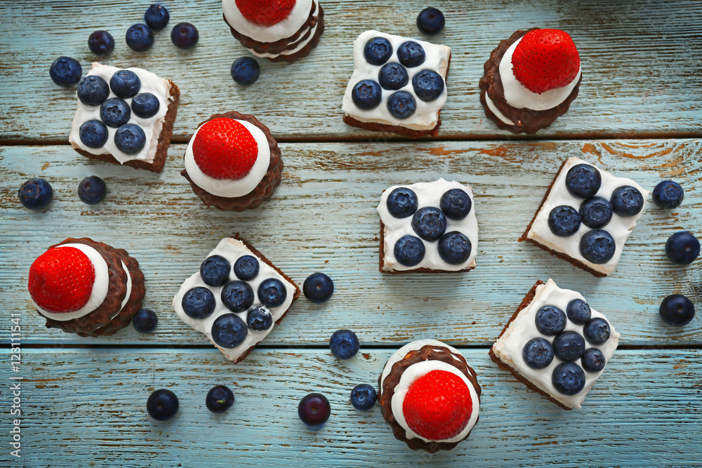 Delicious strawberry and blueberry cakes on wooden table