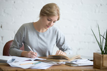 Student Female Performing A Written Task In A Copybook With A Pen, Looking At The Textbook, Education Concept Photo, Horizontal