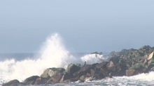 Large Storm Waves Crashing On Rocky Inlet Pier At Pacific Ocean With Seagulls Flying.