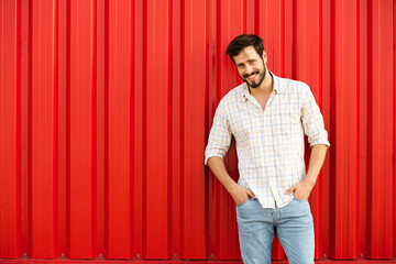 Wall Mural - attractive man smiling and standing o red wall