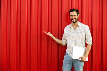 Wall Mural - man presenting one side with laptop in hands on red background