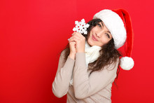 Girl In Santa Hat Portrait With Big Snowflake Toy Posing On Red Color Background, Christmas Holiday Concept, Happy And Emotions