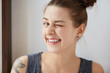 Nice close-up portrait of young European hipster girl with bunch of brown hair and tattoo. Happy tricky cute woman with smiling face blinking at camera in a playful manner. Having fun concept.