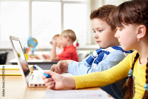 Plakat Dwoje małych dzieci siedzi przy stole w szkole i patrząc na ekranie laptopa