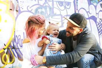 dad in black hat smiles to his daughter hugging her and his woma