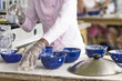Woman preparing food at an outdoor restaurant sprinkling seasoning into one of a group of blue bowls on a table in a close up view of her hands