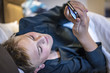 Young boy surfing on his mobile phone with a smile as he relaxes in bed in a close up high angle view
