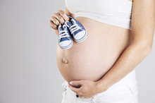 Close Up Of A Beautiful Pregnant Belly With A Pair Of Cute Baby Shoes. Isolated With Light Background.