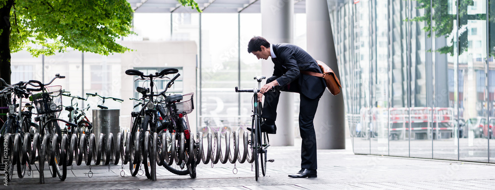 Businessman parking his bicycle in town - obrazy, fototapety, plakaty 