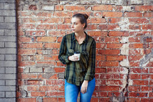 Young Woman In A Plaid Green Shirt Standing Disposable Coffee Cup On The Background  The Red Brick Wall