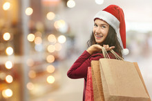 Beautiful Happy Woman In Santa Hat With Shopping Bags On Blurred Market Background. Christmas Shopping Concept.