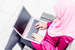 © emiruladzwan - Beautiful young Asian Muslim woman wearing head scarf (hijab) working on a laptop outside the office.