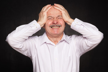 Older man in white shirt hugged his head, wincing.