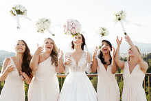 Cheerful Women In Beautiful Gowns Throw Up Wedding Bouquets In T