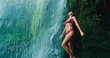 Beautiful young woman relaxing under waterfall