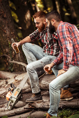 Canvas Print - Two friends Lumberjack worker sitting in the forest and drinking beer.Resting after hard work.