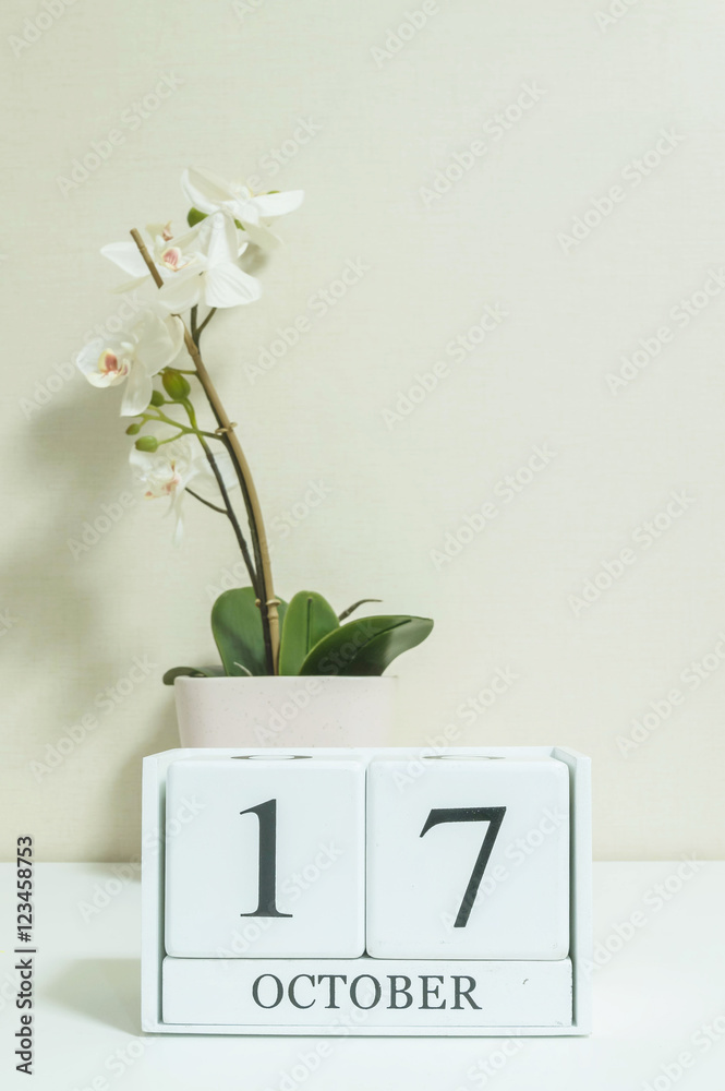 Closeup white wooden calendar with black 17 october word with white orchid  flower on white wood