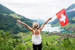 Young woman with swiss flag enjoying great landscape view on the valley with lake and village in Switzerland.