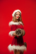 © satyrenko - christmas, x-mas, winter, happiness concept - Bodybuilding. Strong fit woman exercising with dumbbells in santa helper hat , over red background. Muscular blonde girl lifting weights studio shot