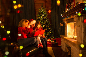 Wall Mural - Happy family reading book at home by fireplace in warm and cozy living room on winter day christmastime