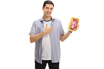 Wall Mural - Cheerful guy holding a steak and pointing