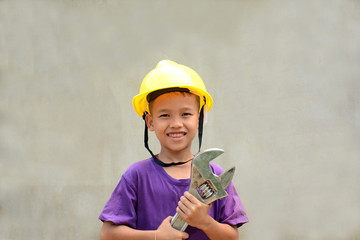 little boy wearing working clothes and holding a wrench .cement gray background