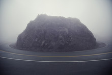 Rock Formation Amidst Country Road During Foggy Weather