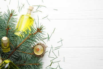 Bottles of coniferous essential oil and branches on wooden background