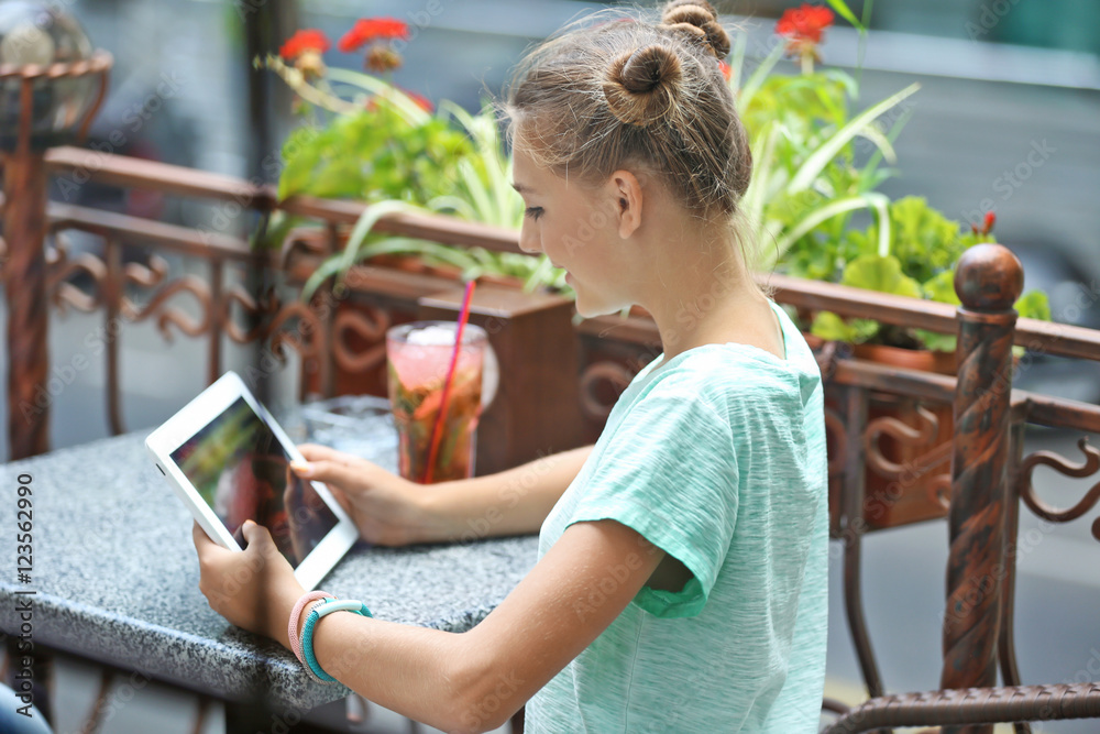 Cute young girl sitting with tablet in cafe