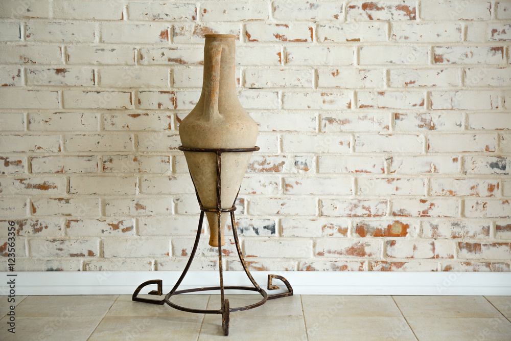 Ancient amphora on stand on brick wall background