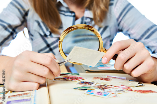 Cuadros en Lienzo Teen girl with magnifier looks his stamp collection isolated