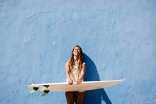 Happy Surfer Girl With Surfboard In Front Of Blue Wall