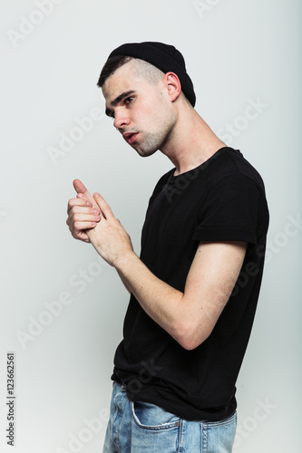 Fotografía Studio shoot of worrying young man wearing black t-shirt jeans and hat rubbing hands