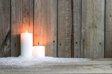 Two white candles in snow by rustic background